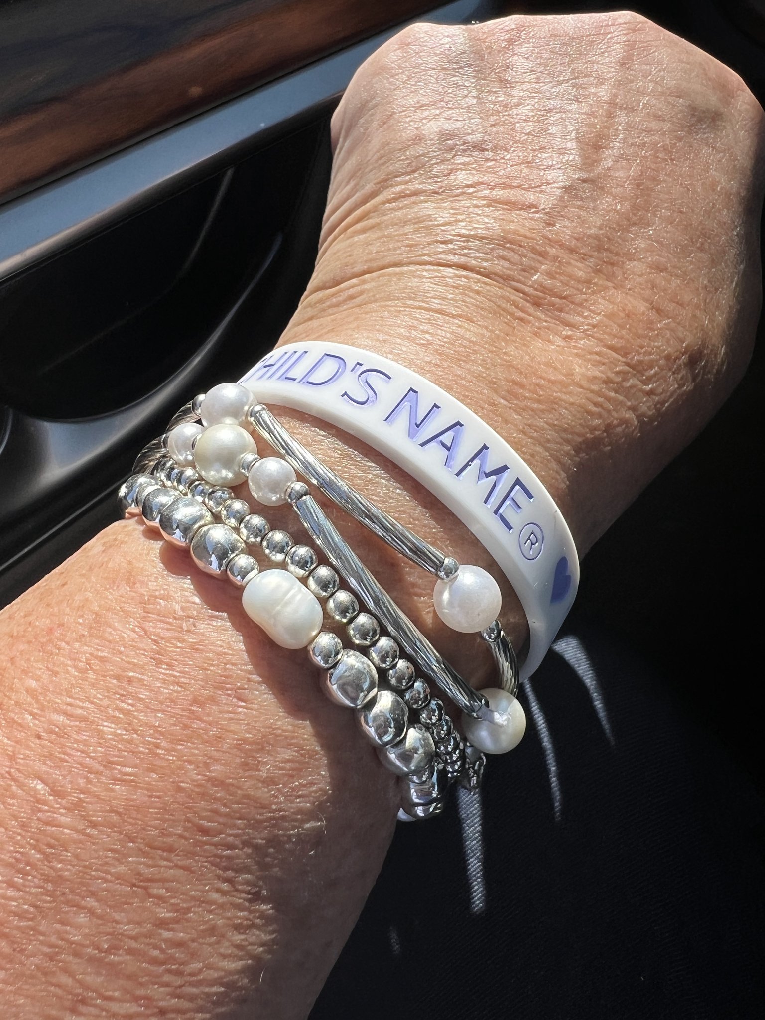 A supporter wearing a Say My Child's Name bracelet with silver and pearl bracelets
